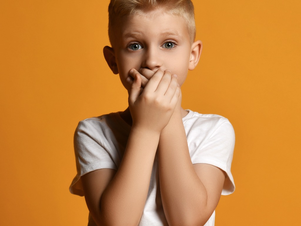 a boy holding his hands over his mouth